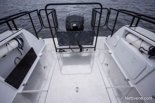 Empty boat deck with metal surfaces, a central outboard motor, and two storage areas on either side. Water visible in the background.